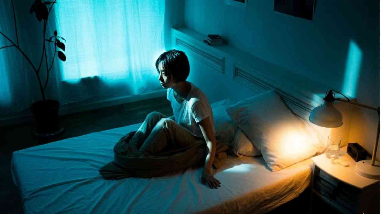 A woman sits on a bed at night in the dark. The image illustrates a moment in which she wonders why she had a nightmare and where dreams come from.