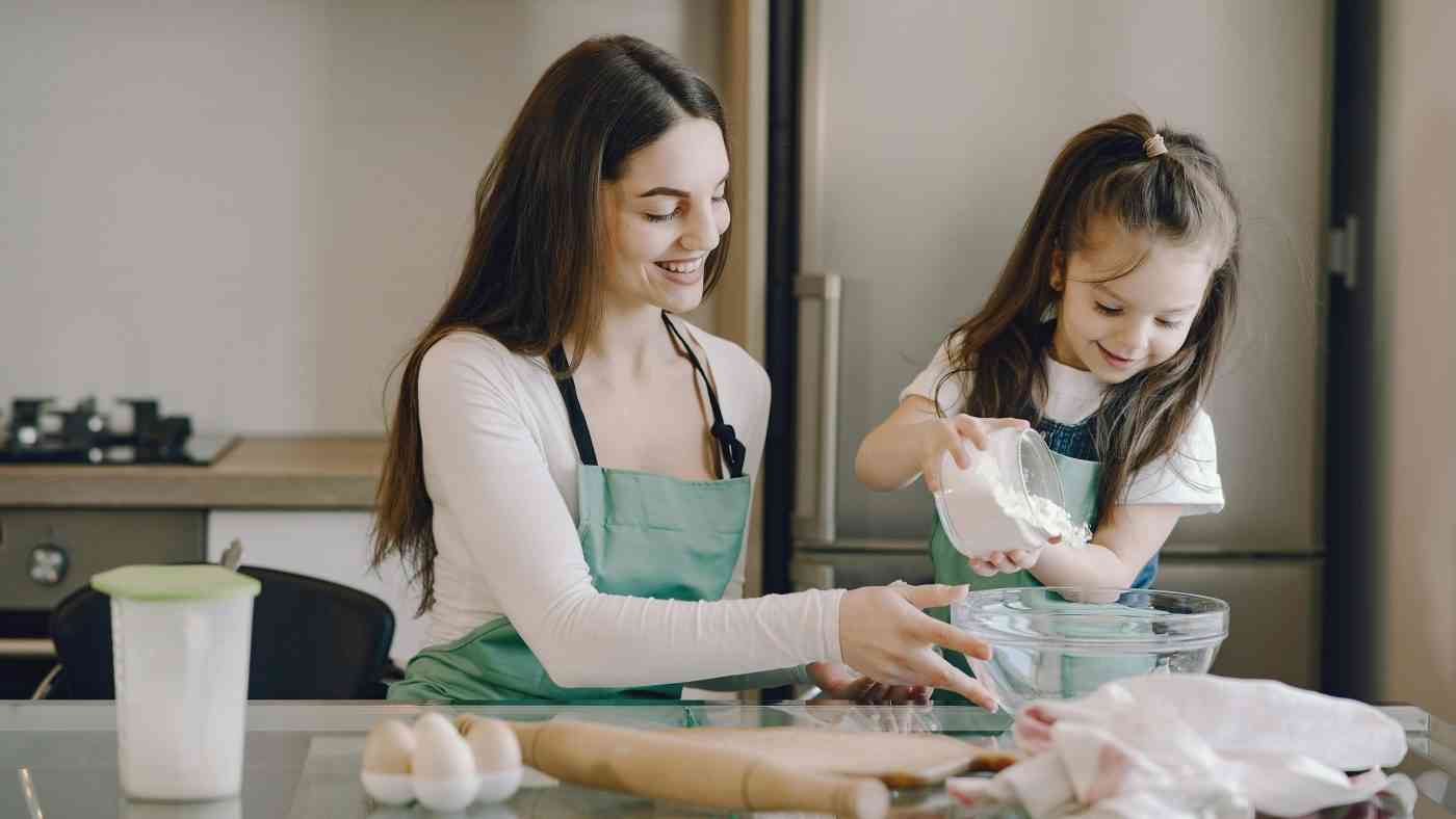 A girl helps her mother in the kitchen, showing the authentic joy of helping in children.