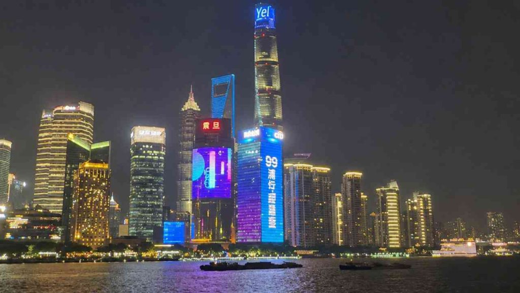 A panorama of Shanghai at night along the river, with illuminated skyscrapers and reflections of lights on the water during a journey to China.