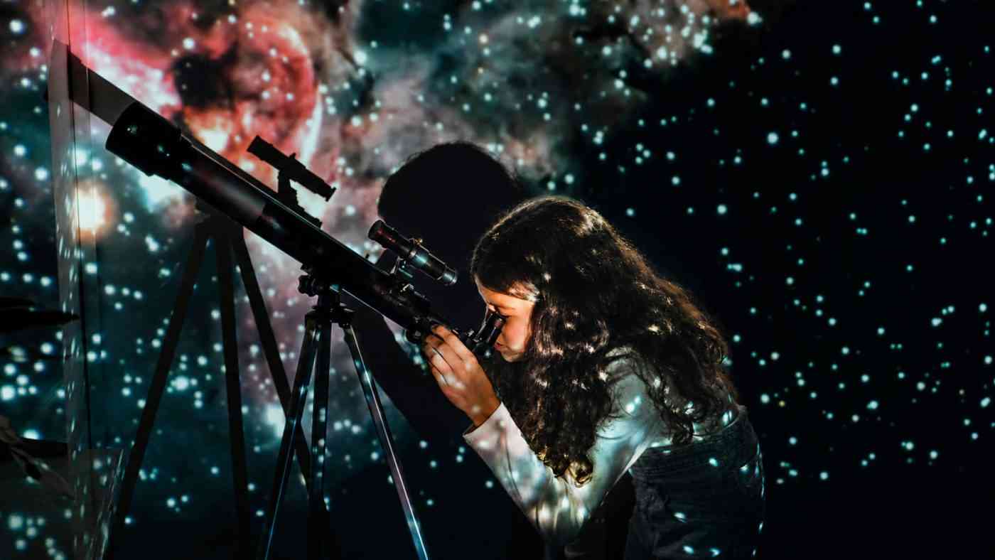 A girl looking through a telescope at the night sky, illustrating how astronomy in school sparks children’s curiosity about the world.