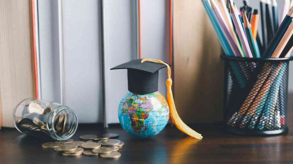 The global war for talent and the emigration of young people, symbolized by a globe wearing a mortarboard, books, coins, and school supplies.