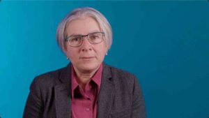 Sharon Levy against a blue background, shown in a medium-wide shot.