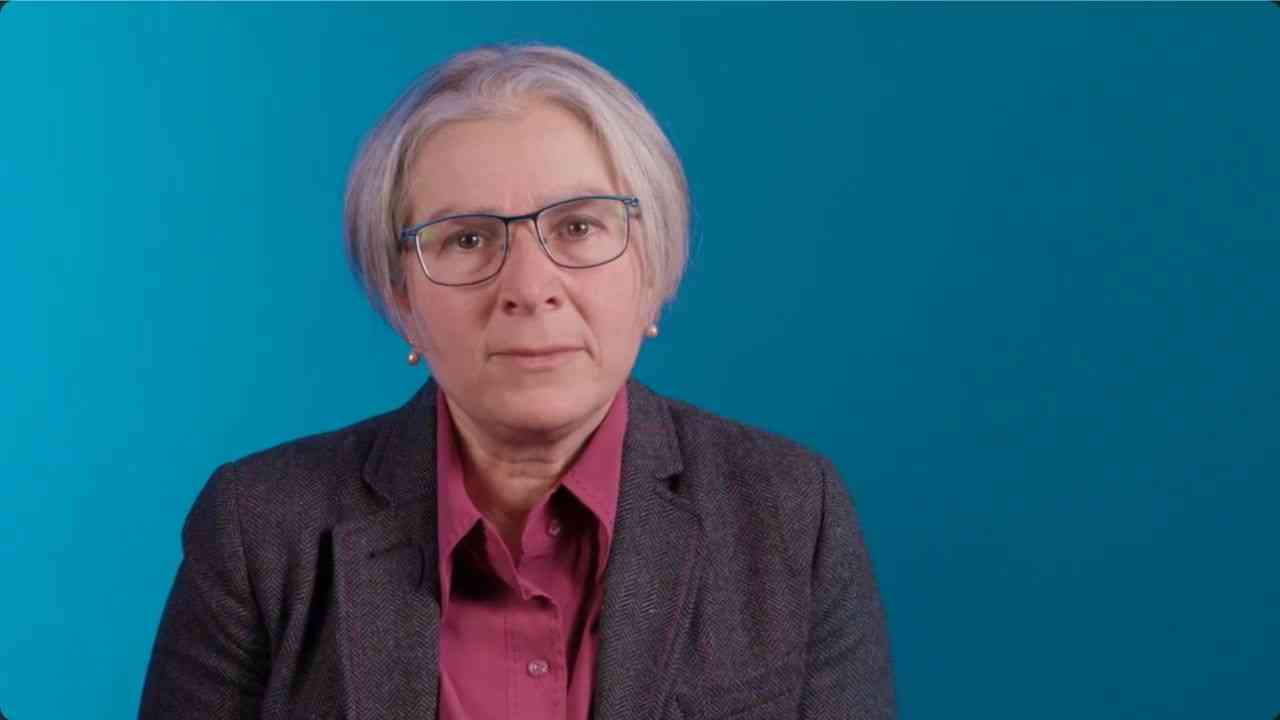 Sharon Levy against a blue background, shown in a medium-wide shot.