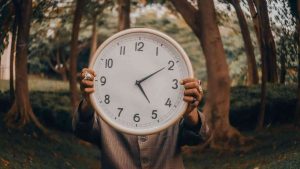 A man is holding a clock and wondering what time is, with a forest in the background.