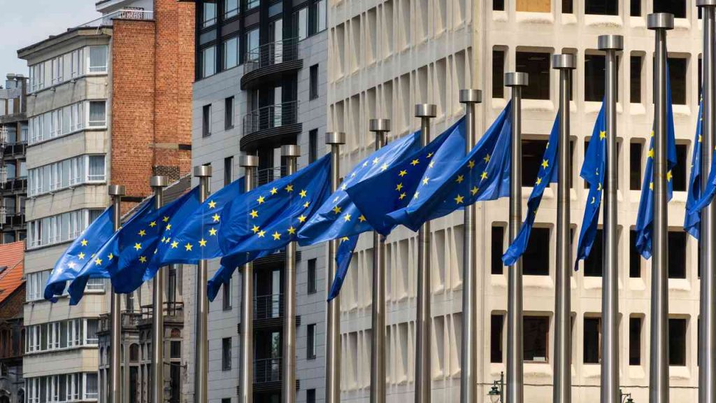 Flags of the European Union in front of the headquarters of EU institutions in Brussels. The image illustrates a text asking whether the EU crisis stems from excessive centralization and which EU reform could determine the future of the European Union.