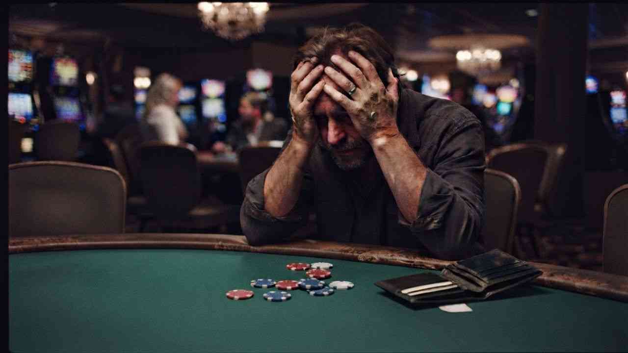 A devastated man at a green table with chips and a wallet, showing gambling addiction.