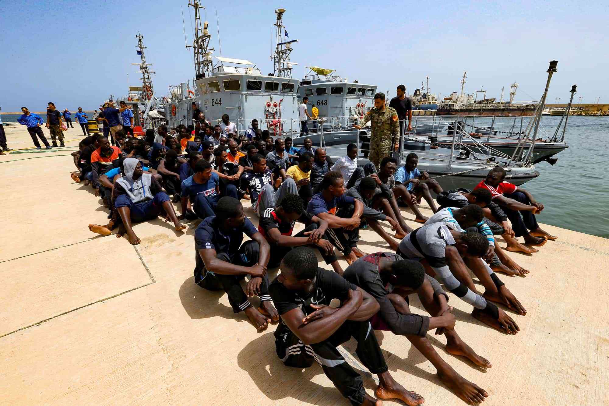 FILE PHOTO: Migrants sit at a naval base after being rescued by Libyan coastguards in Tripoli