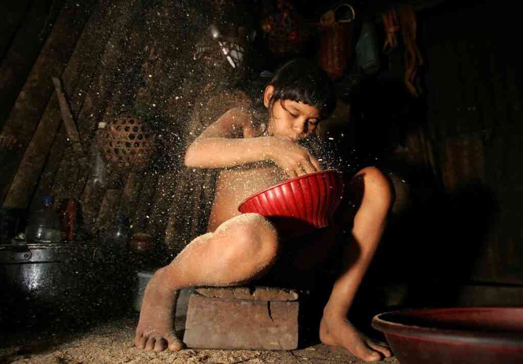 A young indigenous Joti Indian blows to clean rice inside of his shack in the small town of Cano Iguana, Venezuela, Thursday, Oct. 27, 2005. Deep in the jungles of southern Venezuela, Indians wearing loincloths and beaded necklaces gather in a hut to hear their leader explain why the American missionaries who help them are being told to leave the country. (AP Photo/Fernando Llano)