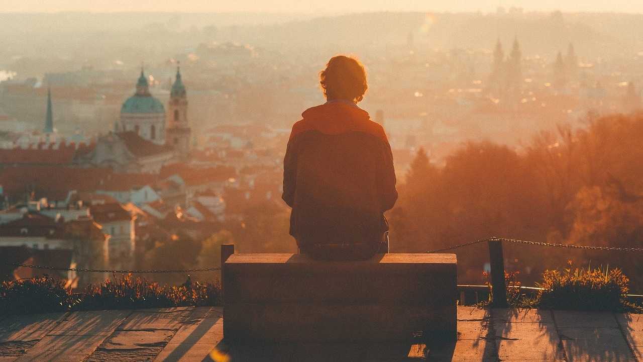 zmierzch humanizmu, człowiek w samotności siedzacy na ławce, spogląda na miasto w tle o zachodzie słońca.