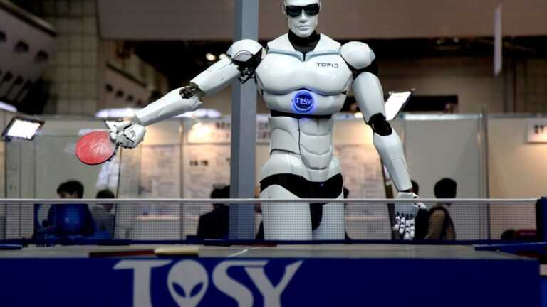 Chińskie roboty humanoidalne. Humanoidalny robot w okularach przeciwsłonecznych gra w tenisa stołowego na targach technologii.