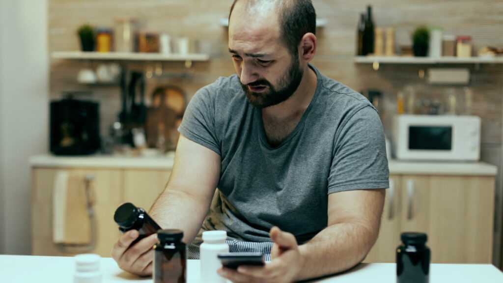 Szkodliwe reklamy leków: mężczyzna trzyma w jednej ręce telefon, a w drugiej trzyma opakowanie na leki