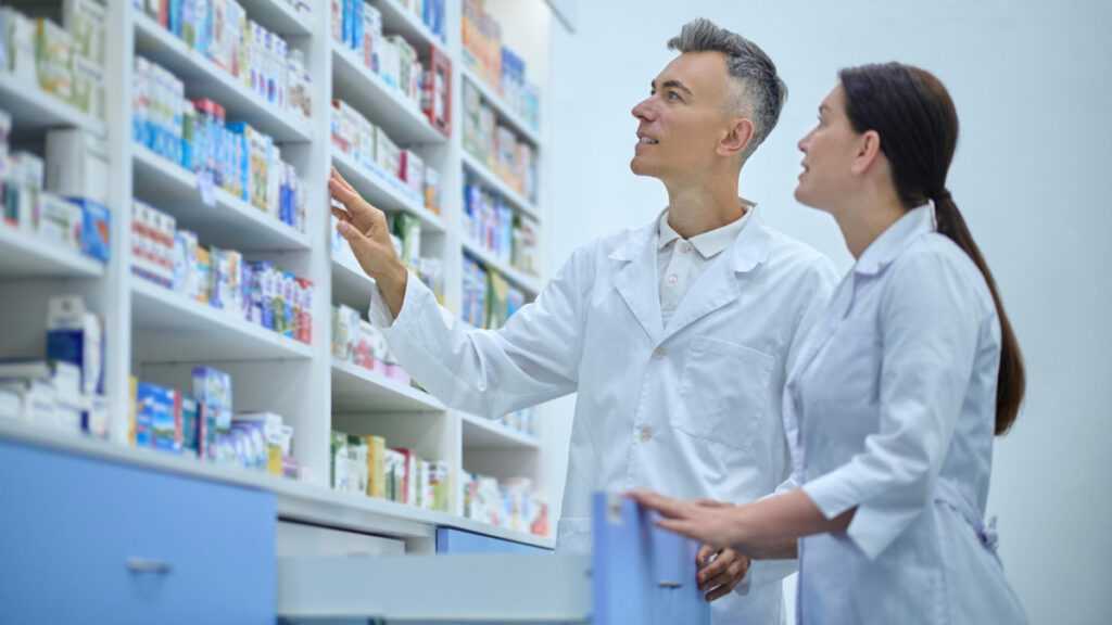 Szkodliwe reklamy leków: farmaceuta i farmaceutka w aptece przy półce z lekami