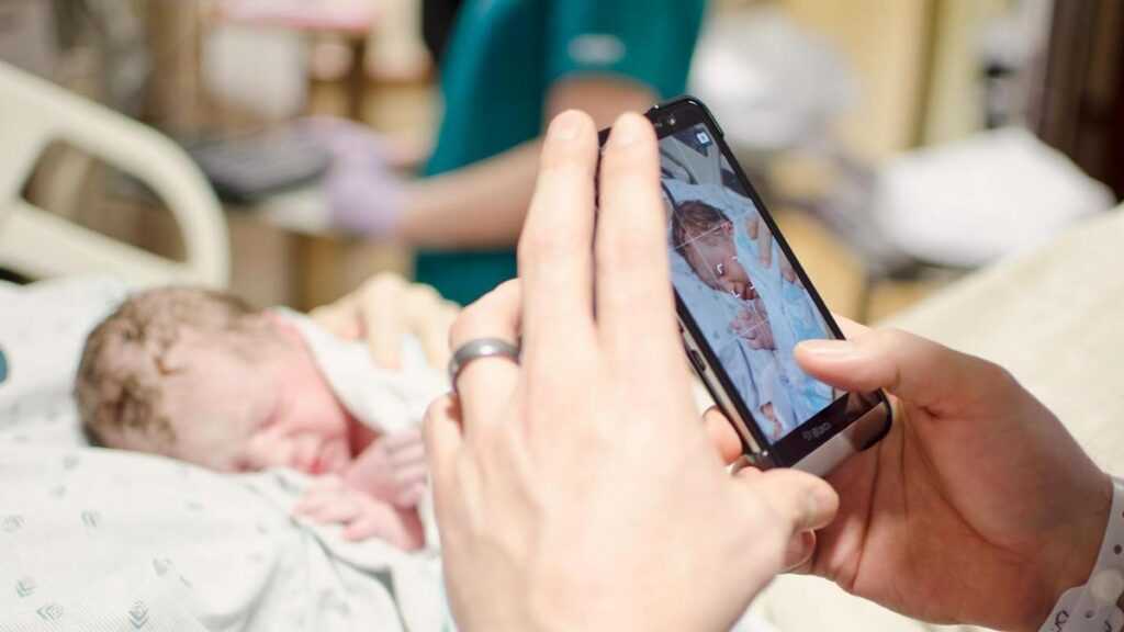 Zagrożenia sharentingu: zbliżenie smartfona, którym kobieta robi zdjęcie noworodka