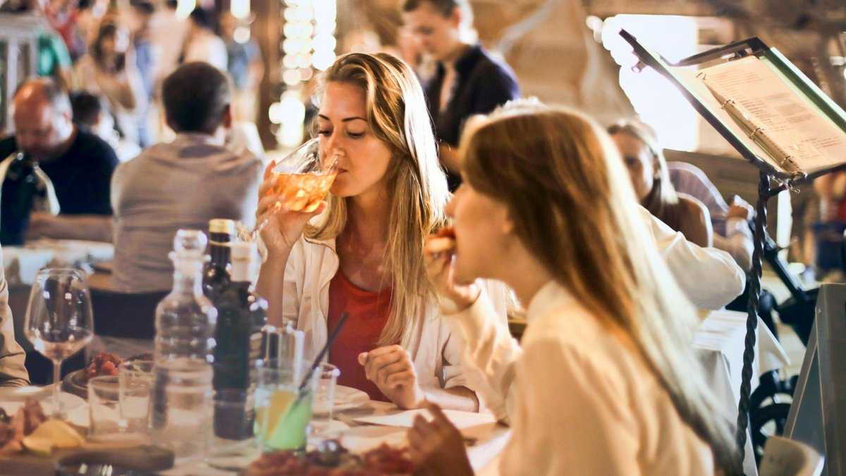 Godziny posiłków w diecie, Fot. Andrea Piacquadio/pexels. Dwie kobiety jedzą i piją w gwarnej restauracji, delektując się posiłkiem w towarzystwie.