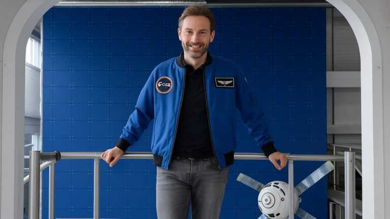 polskie eksperymenty na ISS, Fot. Polsa, Astronauta Sławosz Uznański w niebieskiej kurtce stoi na tle modułu treningowego ISS.