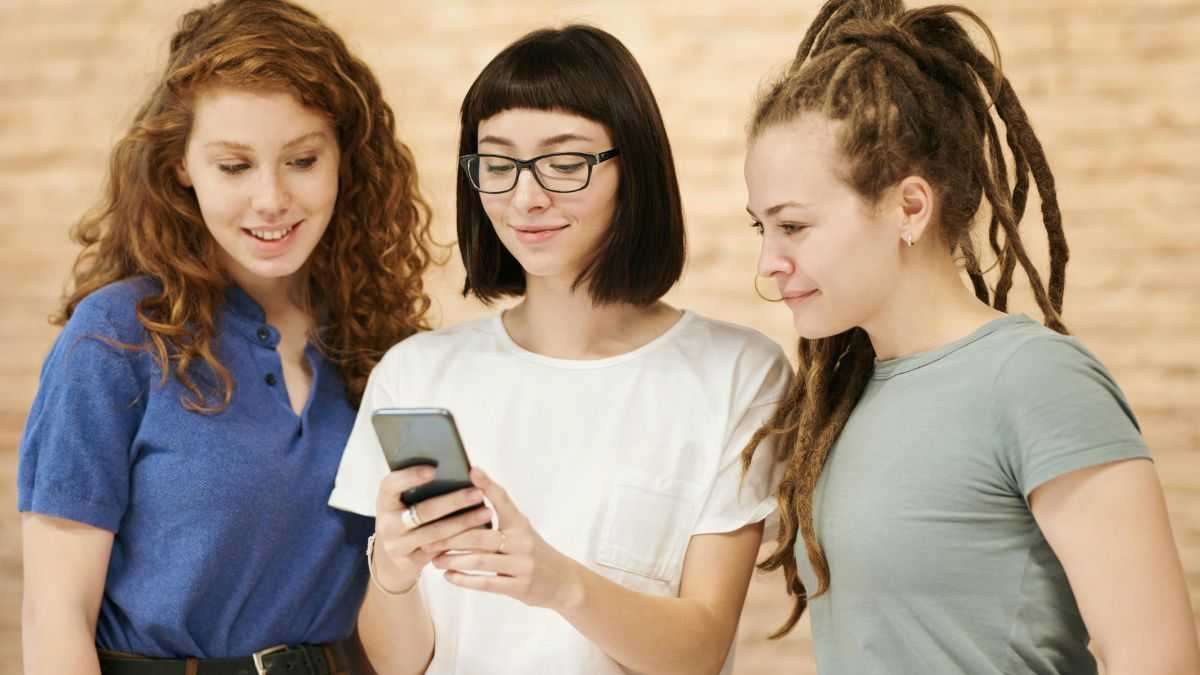 pomoc mediów społecznościowych: trzy uśmiechnięte młode kobiety patrzą w jednen smartfon