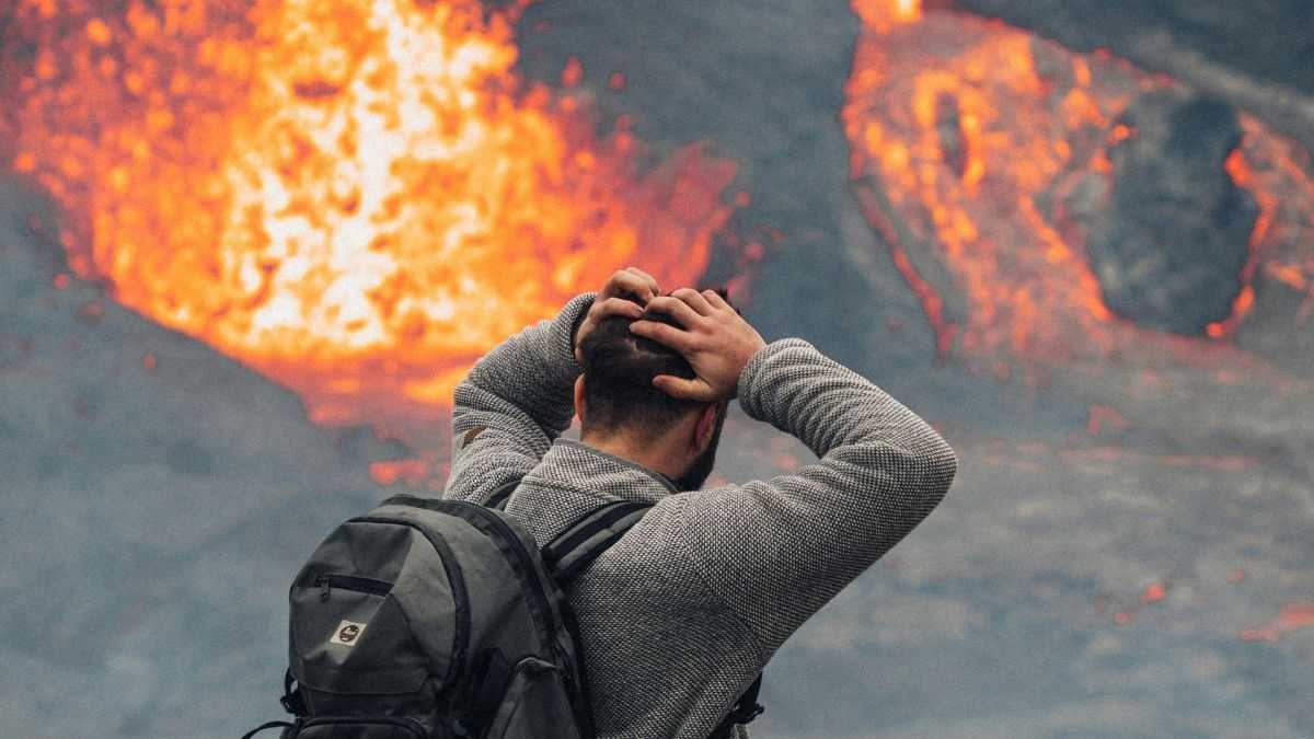 prognozy nadchodzących kataklizmów: mężczyzna w szarym ubraniu chwyta się za głowę przed nim wybuch wulkanu pomarańczowa lawa