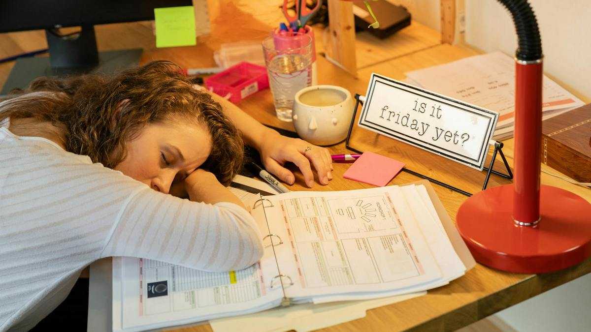 Skutki braku snu: przepracowana kobieta przysypia na biurku w pracy