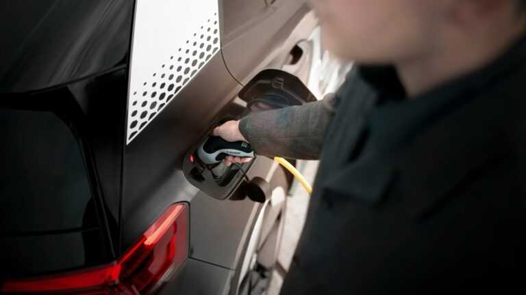 Nowa bateria wodna: mężczyzna ładuje elektryczny samochód za pomocą kabla zasilającego.