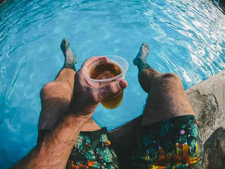 Czy alkohol relaksuje: mężczyzna z nogami w basenie i plastikowym kubkiem z napojem w dłoni. Fot. Derek Owens / Unsplash