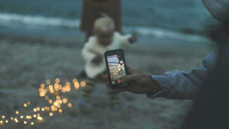 Jakie są zagrożenia sharentingu: mężczyzna robi zdjęcie telefonem małemu dziecku na plaży