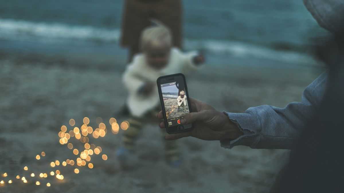 Jakie są zagrożenia sharentingu: mężczyzna robi zdjęcie telefonem małemu dziecku na plaży