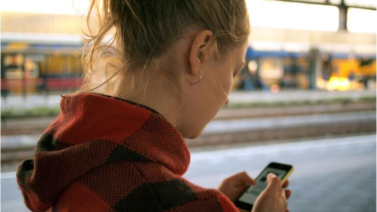limit korzystania z social mediów: blondynka w czerwonej kurtce patrzy na komórkę