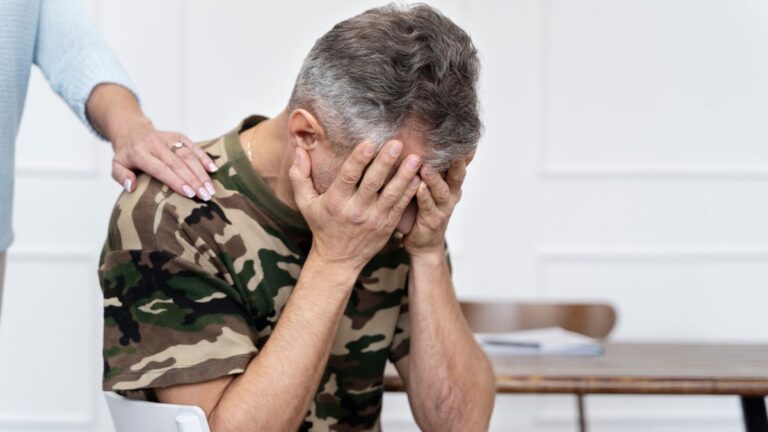 Jak leczyć PTSD: Mężczyzna z ręką w dłoniach siedzi w gabinecie lekarskim, kobieta trzyma mu dłoń na ramieniu. Fot. Freepik