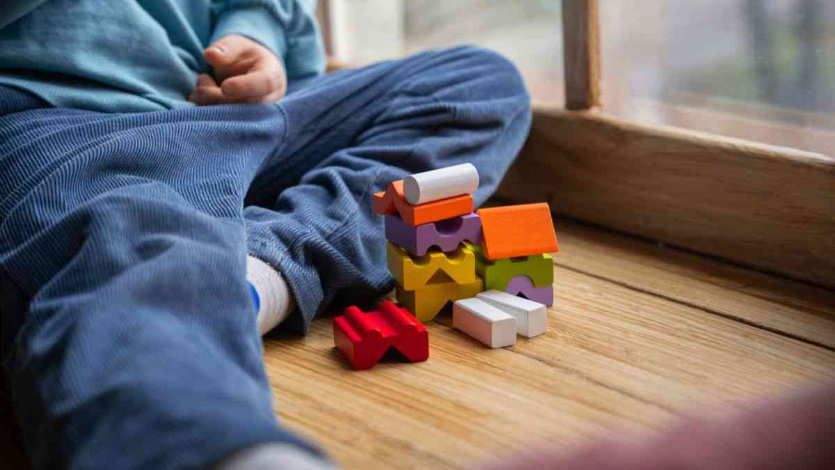 Objawy ADHD u dziecka: Chłopczyk siedzi na parapecie i bawi się klockami. Fot. Freepik