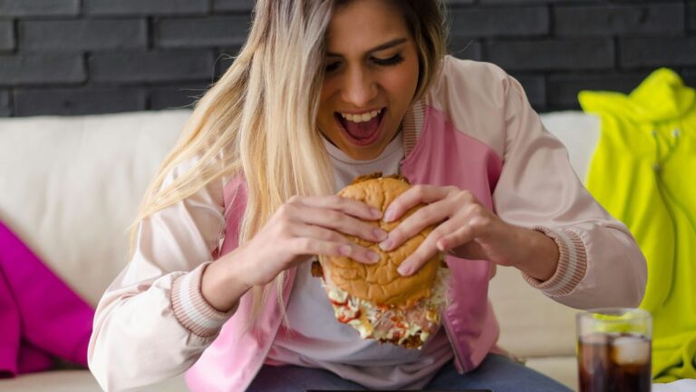 Obsesyjne myśli o jedzeniu: Kobieta zapalczywie je hamburgera. Fot. Frederick Medina / Unsplash.
