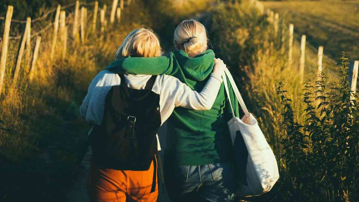 odnowienie przyjaźni: dwie kobiety trzymają się za ramiona i idą obrócone tyłem do kamery polną drogą. Fot. Joseph Pearson / Unsplash