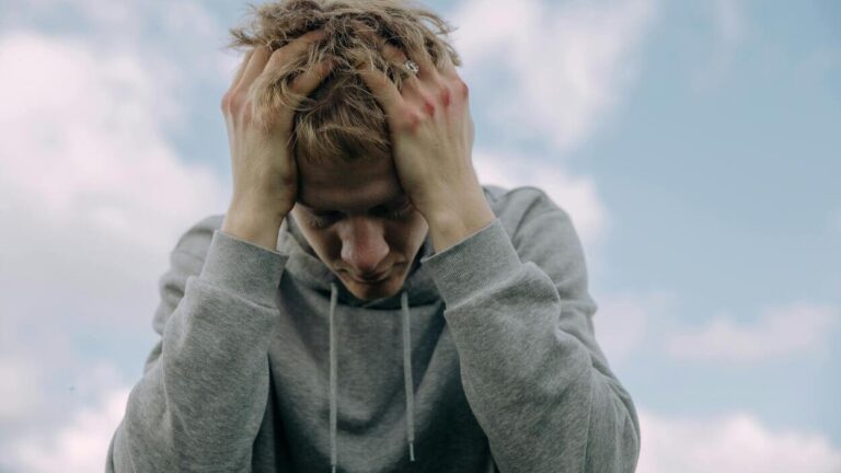 Zmęczony mężczyzna trzymający głowę w dłoniach – połączenie ciała z psychiką; stres a zdrowie psychiczne.