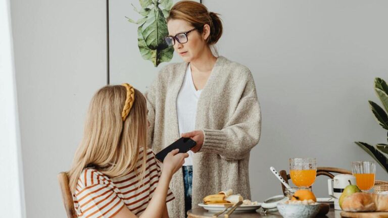 Mama odbiera telefon nastolatce podczas rozmowy o zagrożeniach social media i bezpieczeństwie dzieci w internecie.