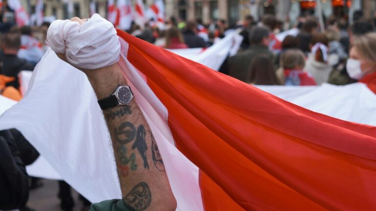 Zaciśnięta pięść z biało-czerwoną flagą podczas protestu, symbolizująca emocje i postawy wobec przemocy politycznej – poglądy polityczne a przemoc, konserwatyzm a wojna, lewicowe poglądy a agresja, psychologia polityki.