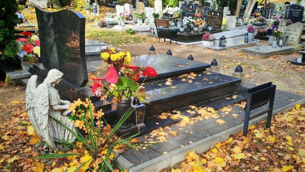 Jesienny cmentarz w Polsce – groby z kwiatami, zniczami i figurą anioła