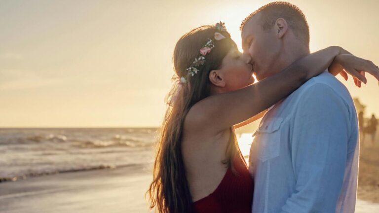 Para całuje się na plaży o zachodzie słońca – ilustracja do tematu, dlaczego się całujemy i jaka jest historia pocałunku.