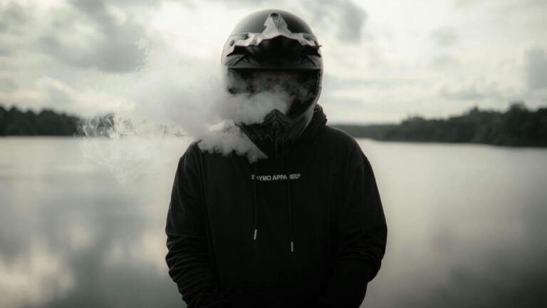 Osoba w kasku na tle jeziora otoczona gęstą chmurą aerozolu, używana jako ilustracja do tematu, jak szkodzą inhalatory nikotyny.