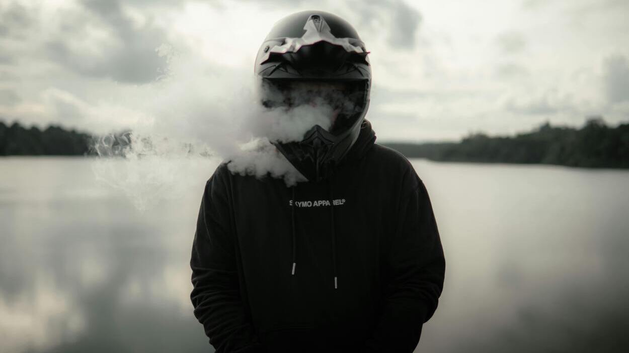 Osoba w kasku na tle jeziora otoczona gęstą chmurą aerozolu, używana jako ilustracja do tematu, jak szkodzą inhalatory nikotyny.