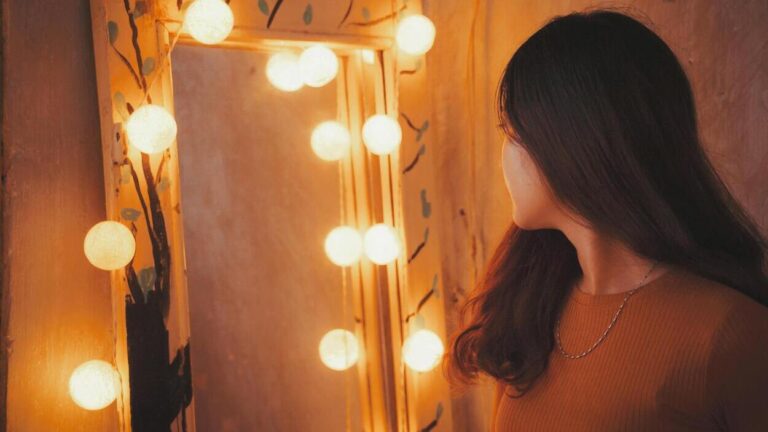 Kobieta stojąca przed lustrem, patrząca na swoje odbicie — symboliczna scena ilustrująca narcyzm u nastolatków.