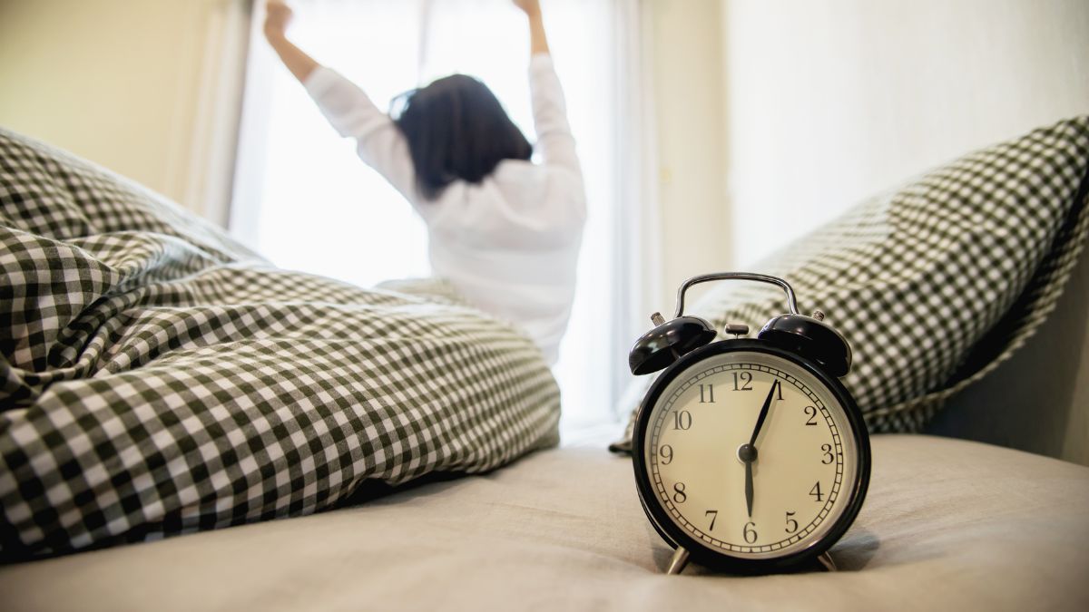 Odporność organizmu rano: budzik leży na łóżku, w tle kobieta właśnie wstaje. Fot. jcomp / Freepik