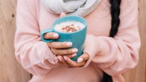 Siedzący tryb życia sposób: kobieta w swetrze trzyma w dłoniach kubek kakao. Fot. Freepik