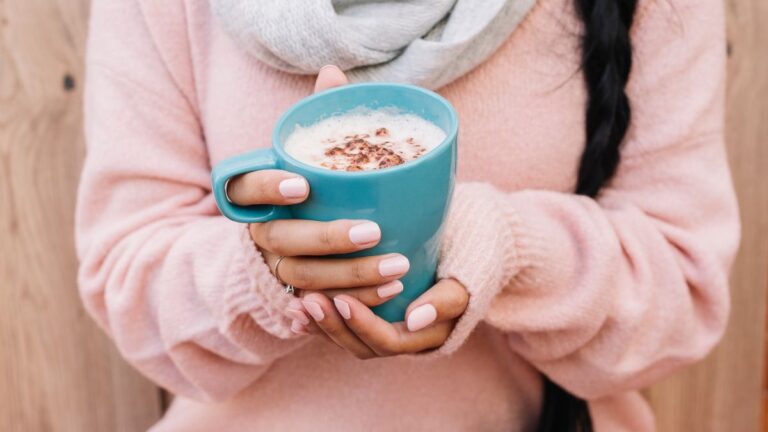 Siedzący tryb życia sposób: kobieta w swetrze trzyma w dłoniach kubek kakao. Fot. Freepik