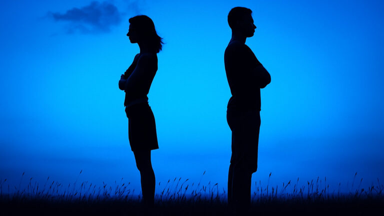 silhouette kobiety i mężczyzny odwróconych do siebie plecami na niebieskim tle, symbolizujących emocjonalne oddalenie i pytanie, skąd bierze się narcyzm