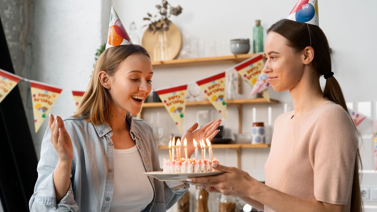 Skąd tort urodzinowy: jedna kobieta wręcza drugiej tort urodzinowy z zapalonymi świeczkami. Fot. Freepik