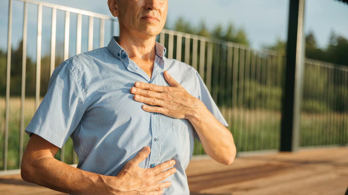 Osoba trzymająca obie dłonie na klatce piersiowej, symbolicznie przedstawiająca skutki choroby Alzheimera oraz związek alzheimera z chorobami serca.
