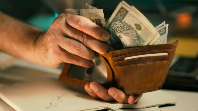 Zdjęcie przedstawia mężczyznę wyjmującego z portfela banknoty, co symbolizuje wypłatę trzynastki pensji i powrót dodatkowego świadczenia dla pracowników.”