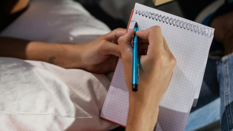 osoba pisze długopisem w zeszycie w kratkę — symboliczne „pisanie na nowo” pod zmiany w języku polskim i nowe zasady pisowni