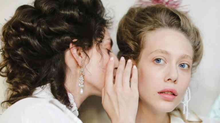 zbliżenie na twarze dwóch kobiet, jedna mówi do drugiej na ucho.