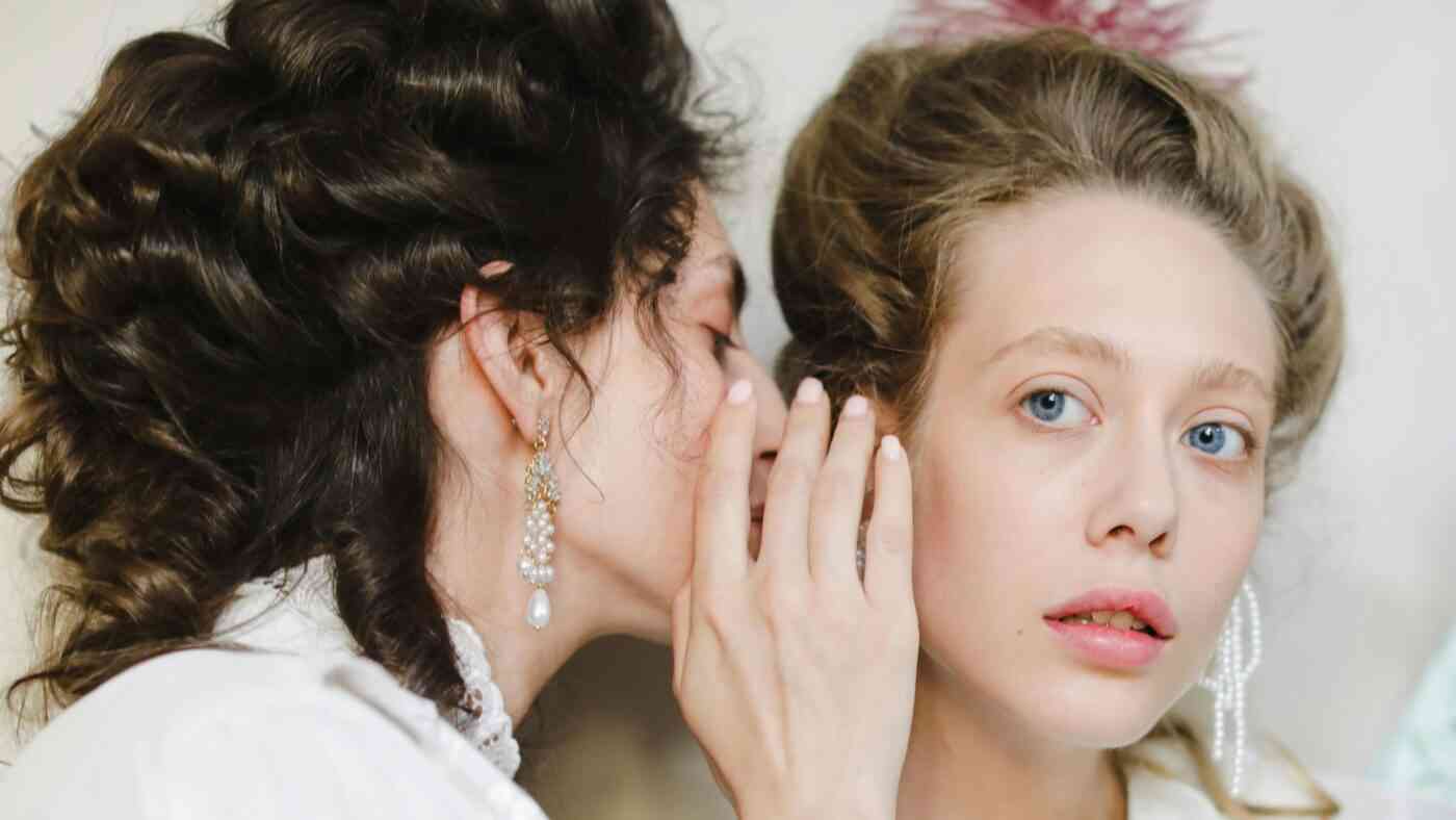 zbliżenie na twarze dwóch kobiet, jedna mówi do drugiej na ucho.