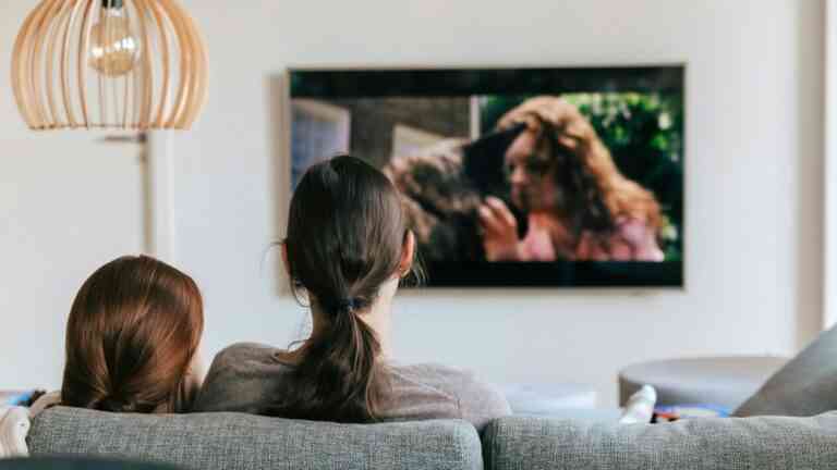 Dwie osoby siedzące na kanapie oglądają film na ekranie telewizora w domowym salonie